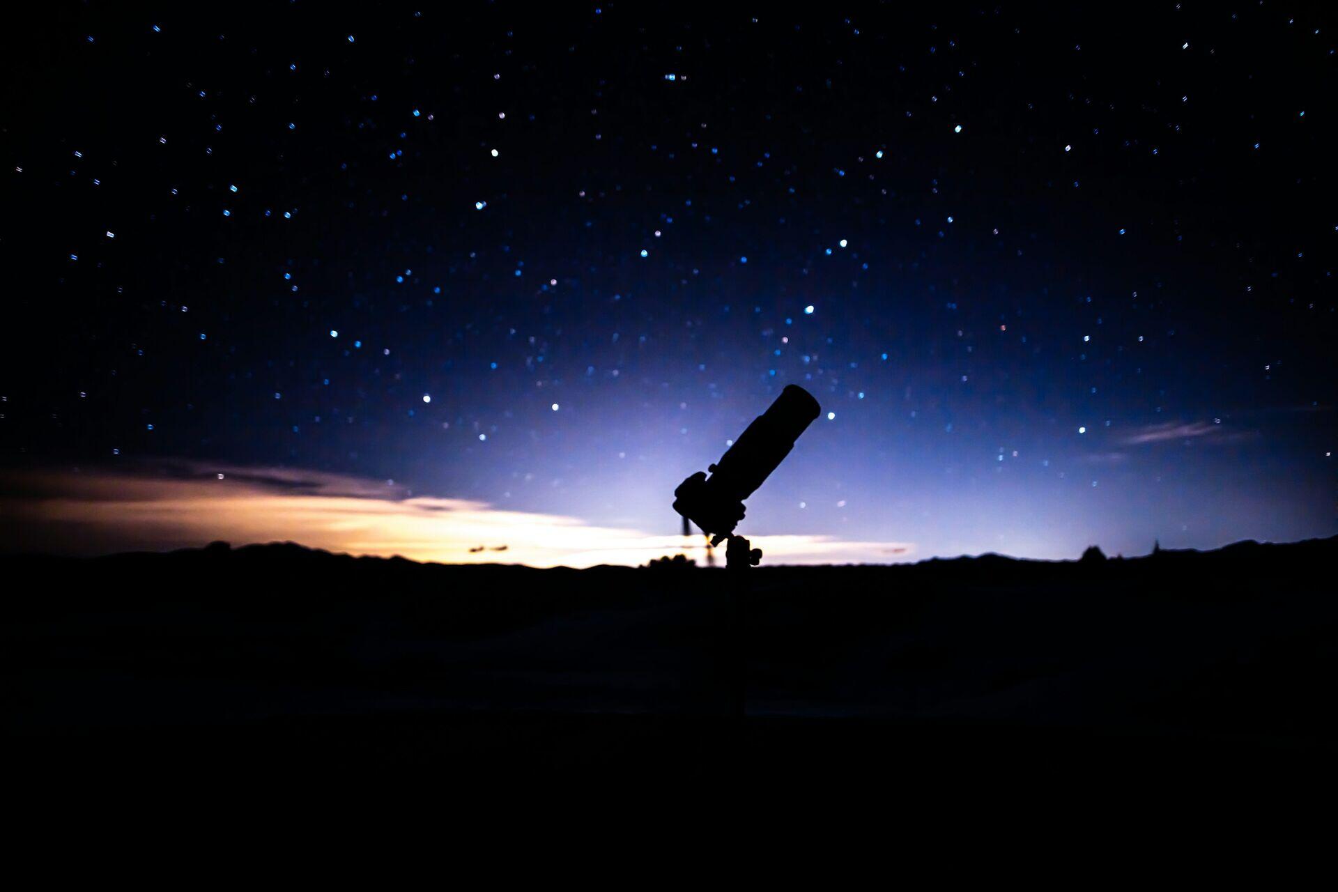 Researcher at a telescope console in a dark observatory room, examining star-field data on a monitor