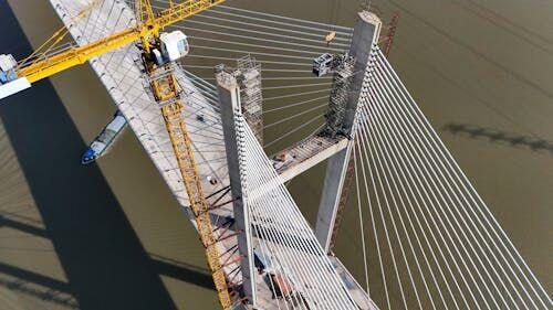 Engineer in hard hat closely inspecting the underside of a steel and concrete bridge over a river