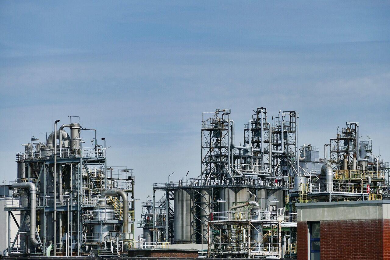 Two workers in hard hats and high-visibility vests examining a large pipeline in a flat industrial field