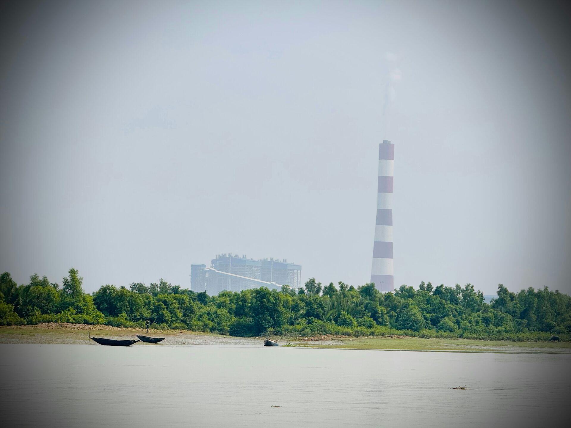 Workers standing near large industrial smokestacks emitting thick grey smoke