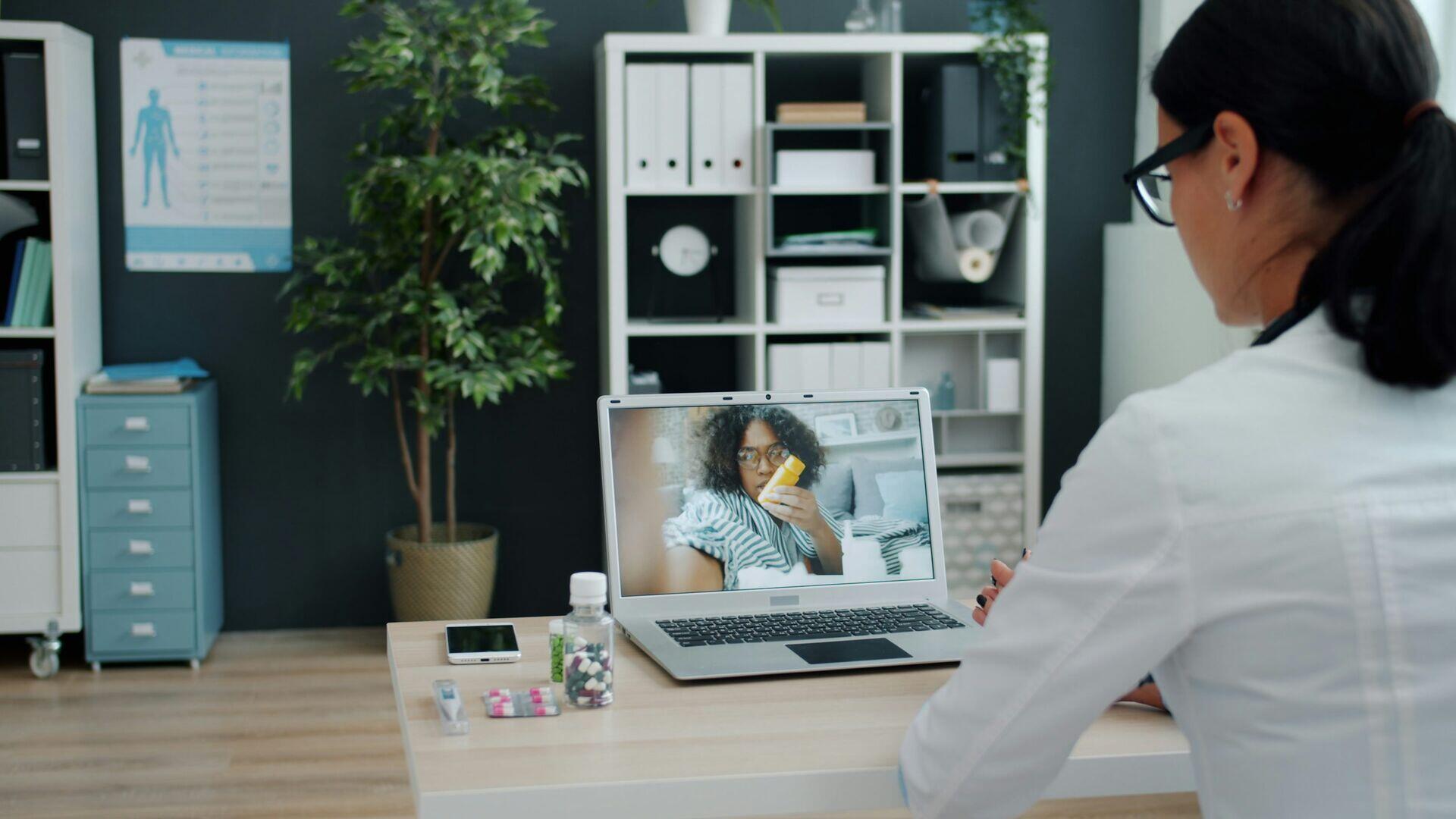 Health worker in a rural clinic holding a tablet showing a video call with a doctor