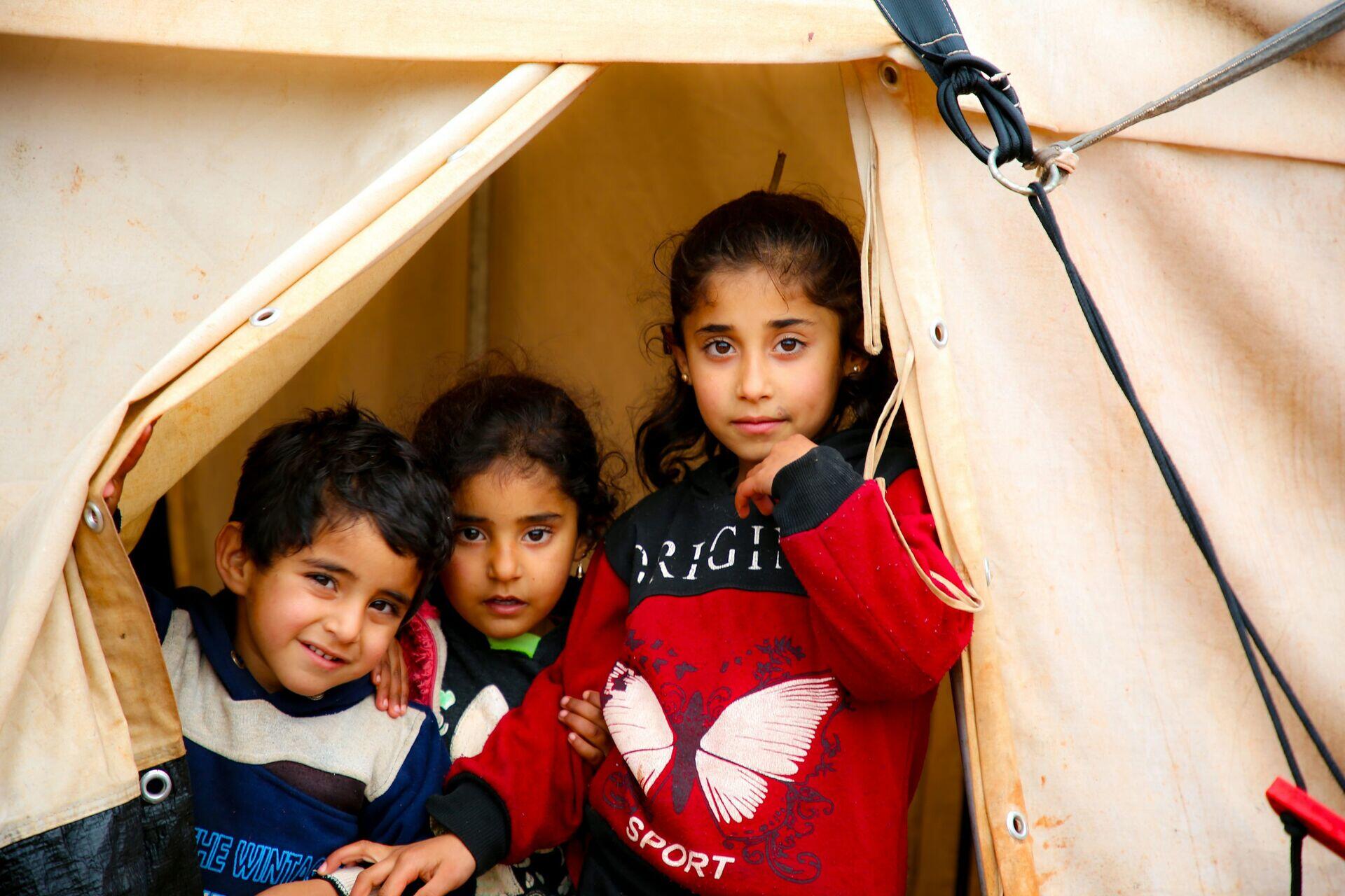Aid worker with tablet registering a refugee family outside a tent in a camp