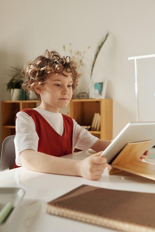 Children sitting at desks with tablets in a rural classroom, a teacher pointing at a screen