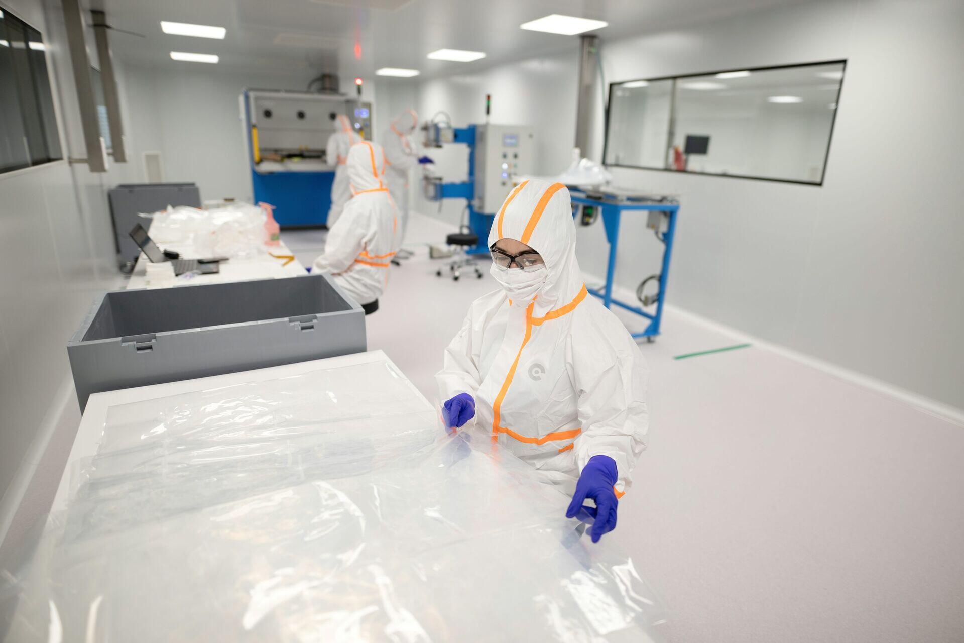 Researcher in lab coat holding and examining a small transparent crystal sample under bright laboratory lighting