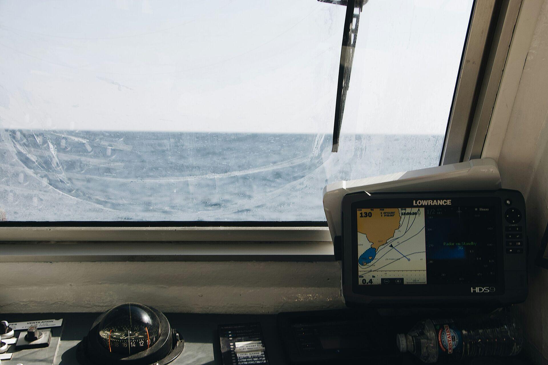 Indonesian fisherman on a small wooden boat looking at a handheld GPS navigation device on open water