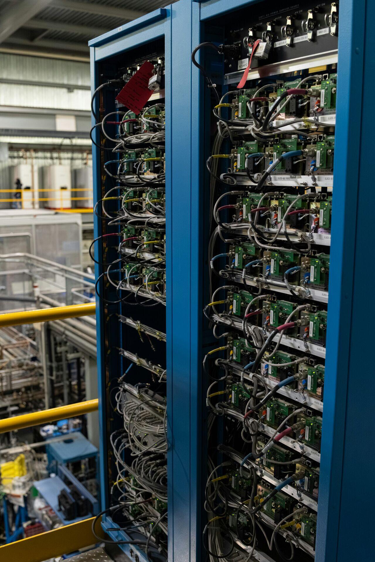 Two engineers in a power grid control room watching banks of screens displaying real-time frequency and clock data