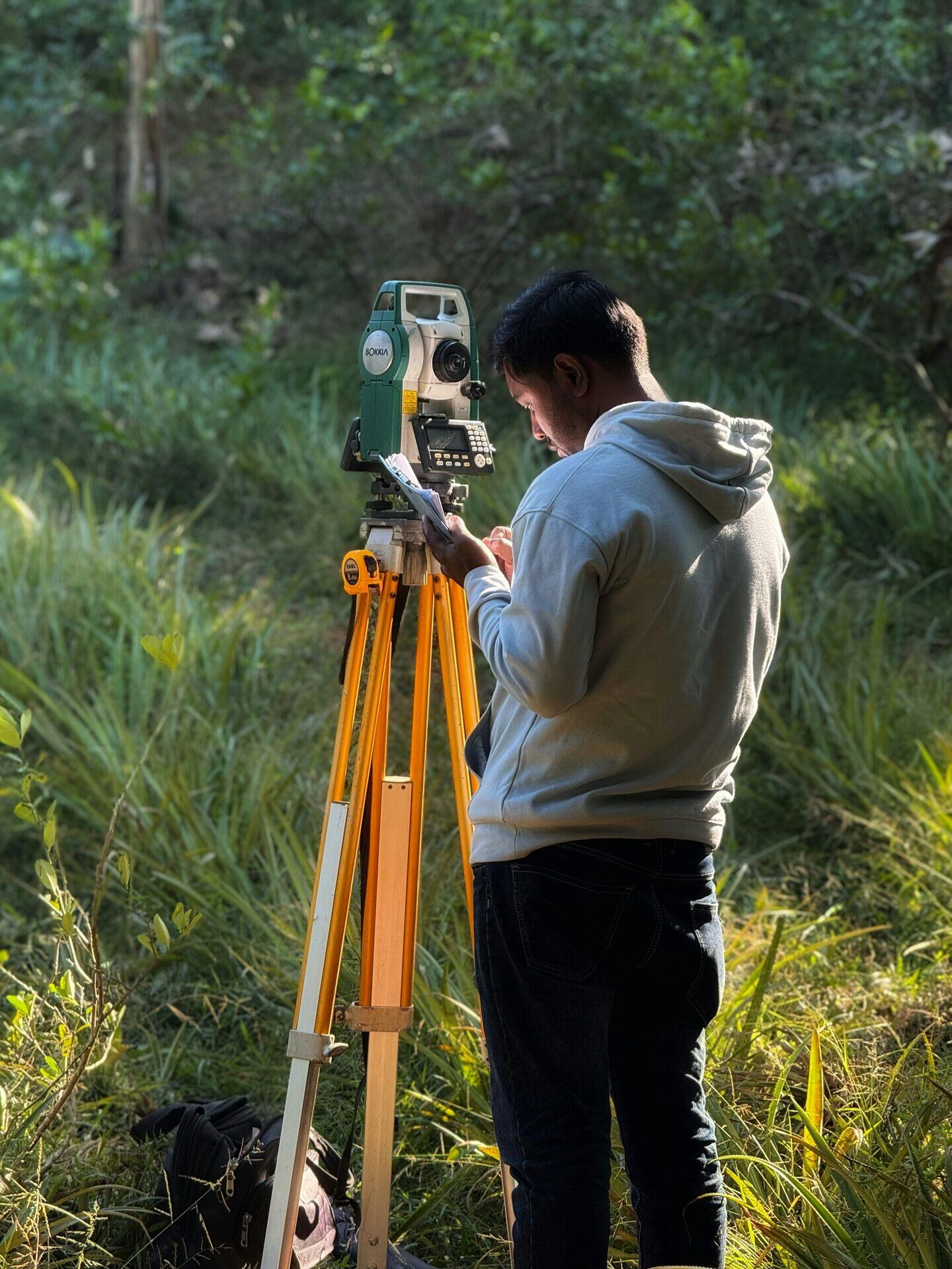 Surveyor holding a GPS rover pole on a tripod in an open field