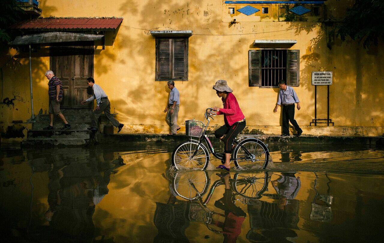 People in a small boat moving through brown floodwater past partially submerged buildings